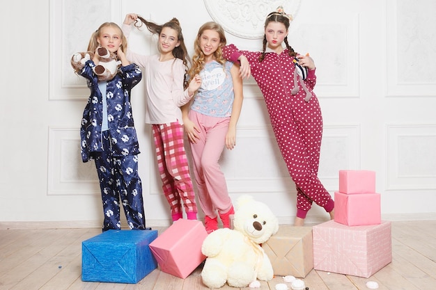 Photo merry christmas and happy new year beautiful happy four child girl in pajamas waiting for a miracle at home with christmas tree little smiling girl with christmas gift box holiday people concept