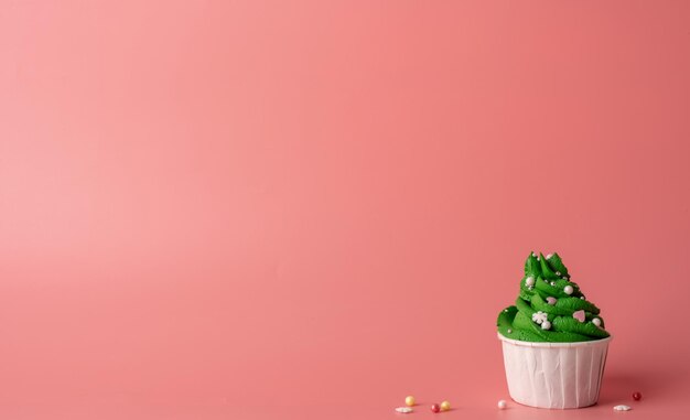 Merry christmas and happy new year. Green Christmas tree shaped cupcakes on pink background. Minimal style, copy space