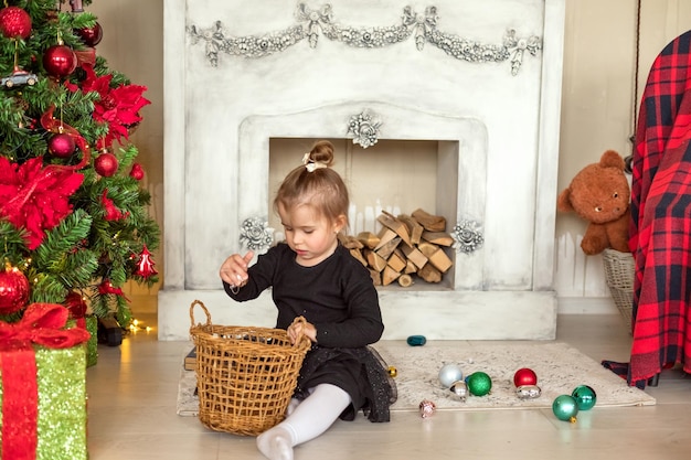 메리 크리스마스 새해 복 많이 받으세요 행복한 어린 소녀는 전통적인 벽난로가 있는 아름다운 거실에서 크리스마스 트리를 장식합니다. 어린이는 크리스마스 이브에 선물을 엽니다.
