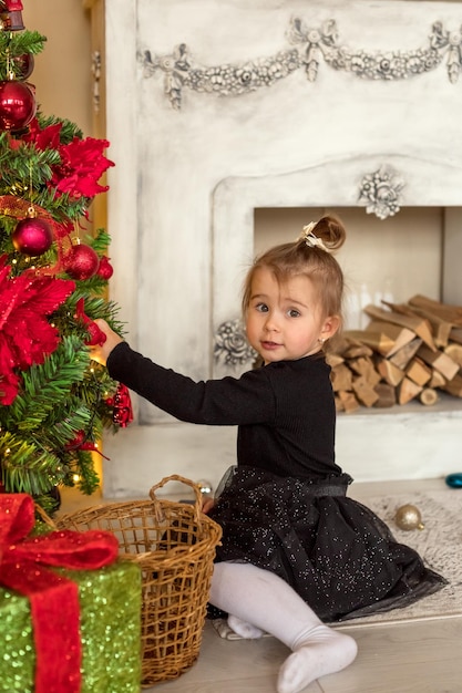 Merry Christmas Happy New Year Happy little girl decorates Christmas tree in beautiful living room with traditional fire place Child opens presents on Xmas eve