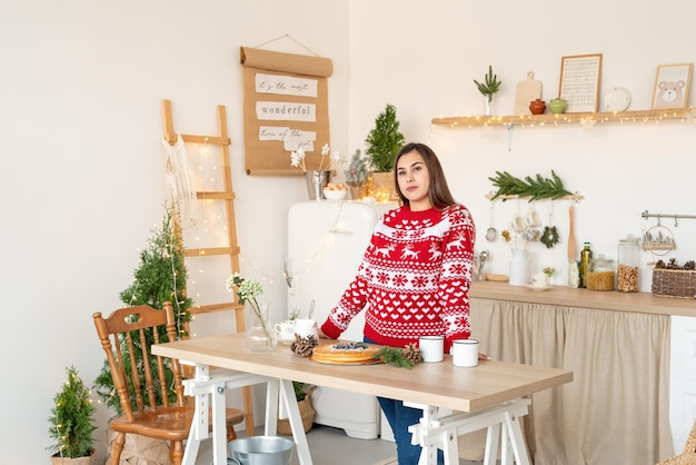 Веселого Рождества и счастливого Нового года. Счастливая молодая брюнетка женщина в рождественском свитере делает горячие напитки на кухне