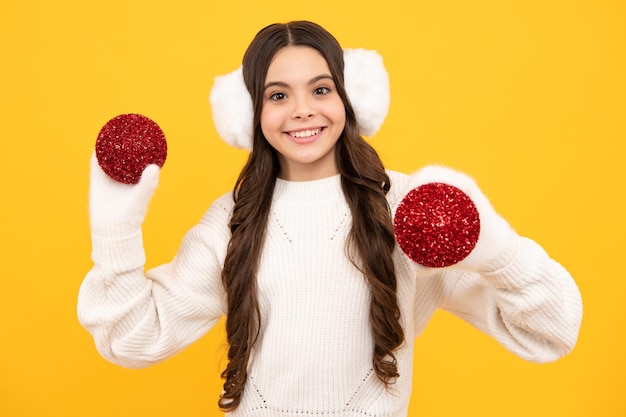 Merry christmas and happy new year portrait of happy teenager\
child wears sweater and knitted gloves on yellow isolated\
background kid in winter clothes teen girl with decorative\
christmas ball