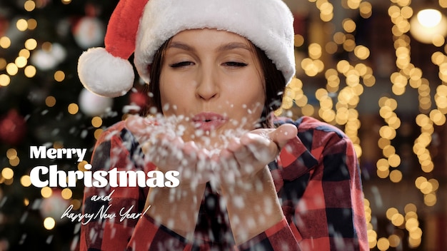 Merry Christmas and happy New Year text. Beautiful woman smiles and blows white snow from her palms straight into camera. Close-up