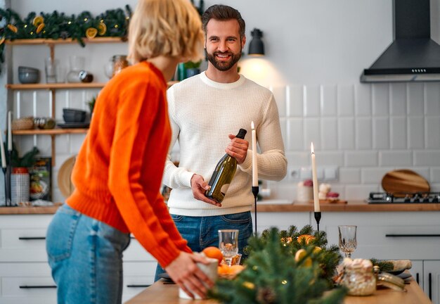 Merry christmas and a happy new year! a young couple in love in the kitchen getting ready laying the festive table, pouring champagne and decorating, waiting for the holiday