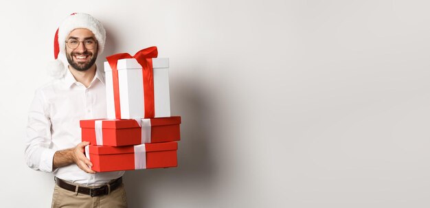 メリー クリスマスの休日の概念幸せな若い男が箱にプレゼントを持って笑顔し、サンタ ハを身に着けています。