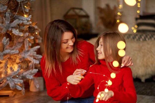 Merry christmas and new year celebrating at home in close family circle. mom and daughter together. magic bokeh from garland lights, shallow depth of field