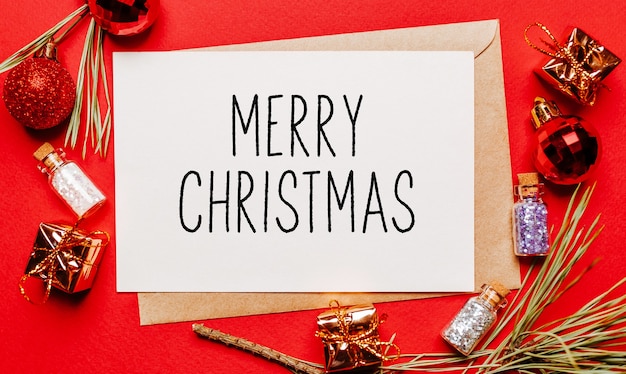 Photo merry christmas note with gift, fir branch and toy on red isolated background. new year concept