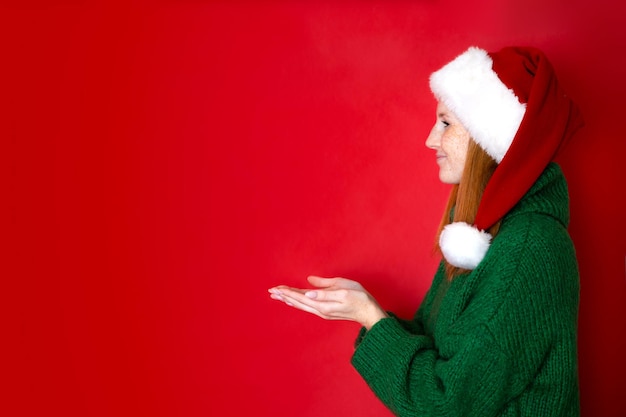 Foto buon natale ritratto di una bella ragazza adolescente in un accogliente maglione verde lavorato a maglia e cappello di babbo natale lo sfondo rosso è il posto per il testo