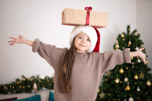 飾られたクリスマス ツリーの背景に彼女の手でギフトを持つかわいい女の子のメリー クリスマスの肖像画