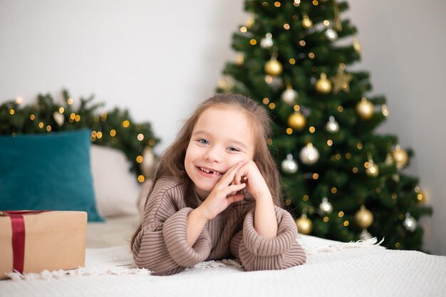 Merry Christmas Portrait of a funny girl with a fallen milk tooth on the background of a Christmas tree with burning lights Lifestyle Space for text