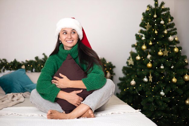 Merry Christmas Portret van een mooie jonge vrouw in een knusse slaapkamer met een versierde kerstboom op de achtergrond Groene trui Lifestyle