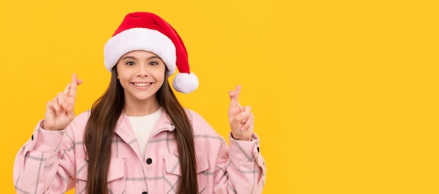 Merry christmas smiling kid in santa claus hat crossed fingers for luck teen girl Banner of christmas child girl studio kid winter portrait with copy space