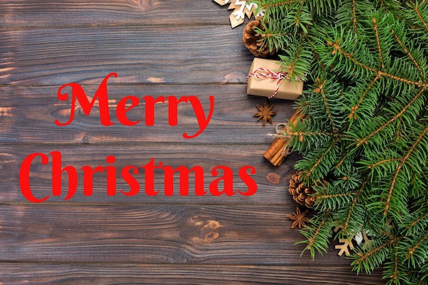 Foto merry christmas-tekst kerstachtergrond met dennenboom en geschenkdoos op houten tafel bovenaanzicht met kopieerruimte voor uw ontwerp