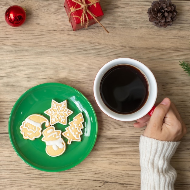 テーブルの上にコーヒーカップと自家製クッキーを持っている女性の手とメリークリスマス。クリスマスイブ、パーティー、休日、新年あけましておめでとうございますのコンセプト