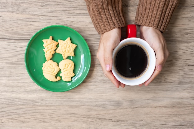 Buon natale con la mano della donna che tiene la tazza di caffè e il biscotto fatto in casa sul tavolo festa della vigilia di natale e concetto di felice anno nuovo