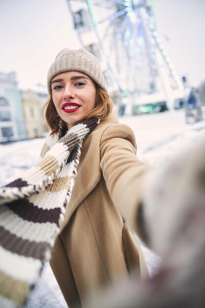 Merry pretty woman taking selfie on snowy day outdoors