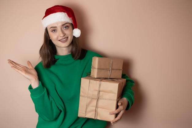 Merry surprised young woman wear xmas sweater Santa hat posing pointing hands arms aside indicate on workspace area isolated on plain pastel light green background Happy New Year 2023 holiday concept