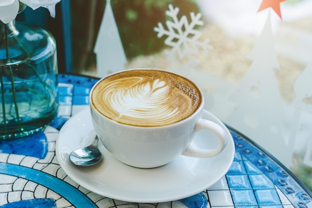 Merry xmasHot coffee latte with latte art milk foam in cup mug with Xmas decors and Xmas tree baubles on marble floor desk Celebrating Merry Christmas and New year