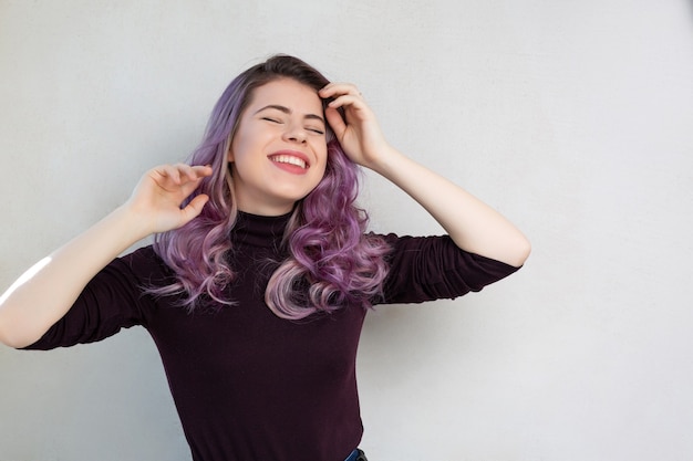 Merry young model with curly purple hair dreaming, isolated on gray background. Space for text