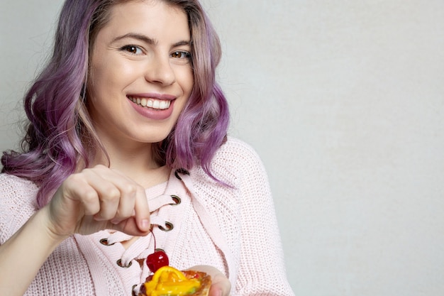 Merry young model with purple hair enjoying tasty dessert with berries. Space for text