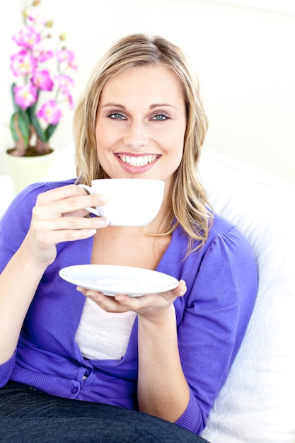 Веселая молодая женщина с чашкой кофе на диване