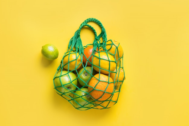 Mesh bag with fruits on yellow. 
