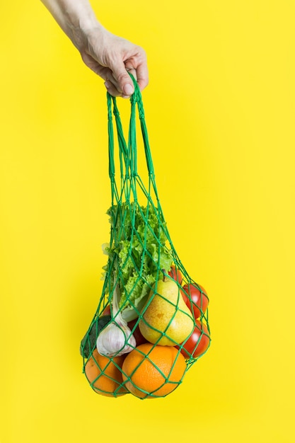 Mesh bag with vegetables in woman's hand. 