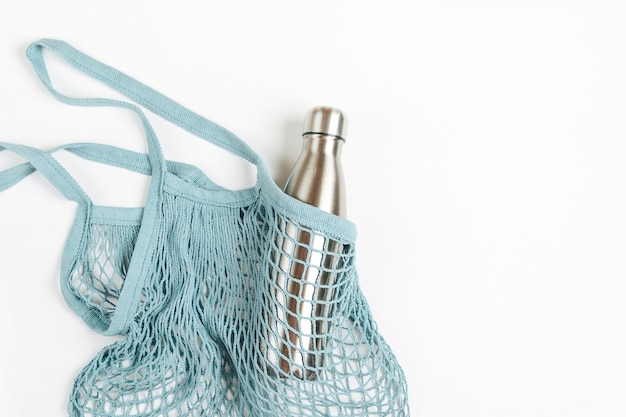 Mesh bags with reusable metal water bottle on white background. Sustainable lifestyle.  