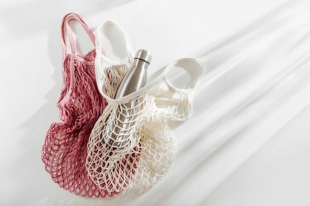 Mesh bags with reusable metal water bottle on white background.
sustainable lifestyle.