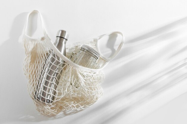 Mesh bags with reusable metal water bottle on white background. Sustainable lifestyle.  