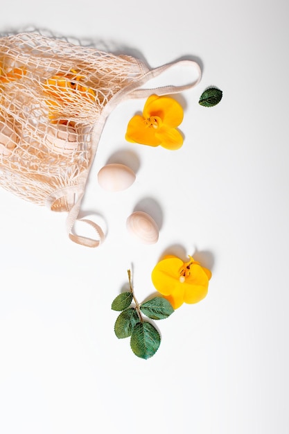 Foto shopper a rete con uova e fiori su sfondo bianco carta di buona pasqua con fiori e foglie verdi