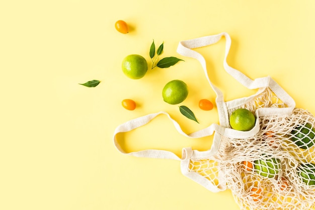 Mesh shopping bag with lyme on yellow background Pattern made of summer tropical fruits Food concept Flat lay top view