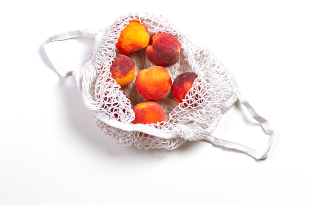 Mesh shopping bag with peaches on white background