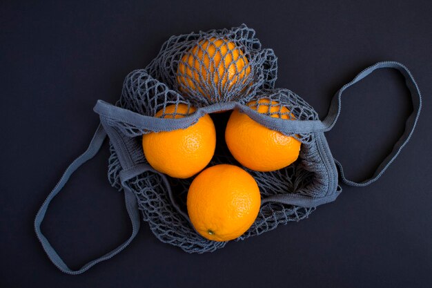 검정 배경에 오렌지가 있는 메쉬 쇼핑 회색 가방비닐 봉투 개념 없음 위쪽 보기 복사 공간
