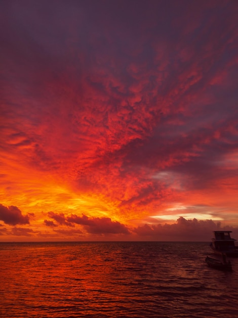 Mesmerizing scene of silhouetted boat in the water against an orange cloudy sky at sunset