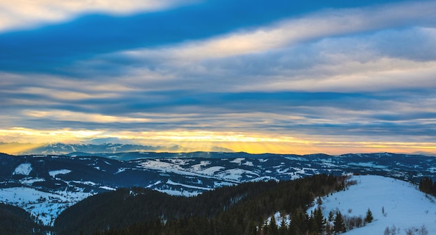 Mesmerizing views of snow-covered mountain ranges against the backdrop of sunset and cloudy cloudy sky. Place for advertising. Winter mountain recreation concept