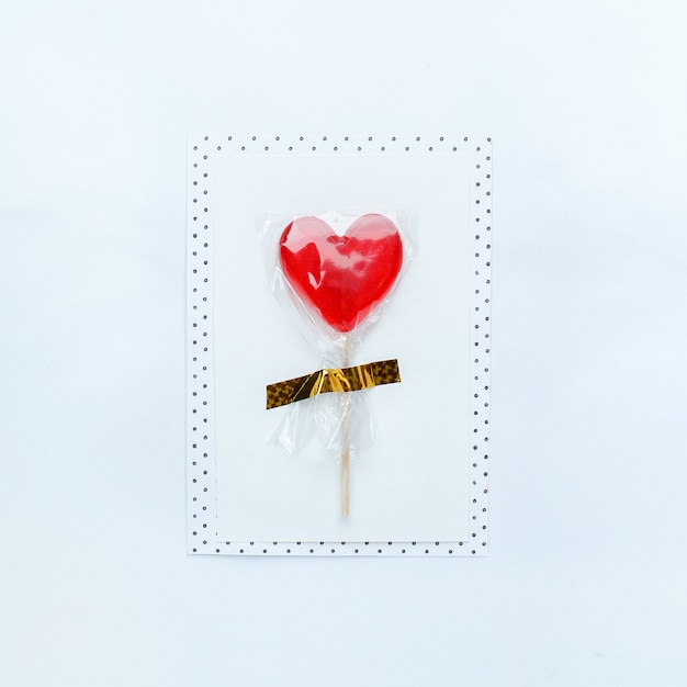 Message card with sugar red heart lollipop on white table.