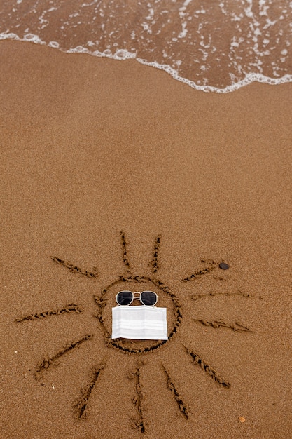 A message in the sand painted sun on the sand the seashore sunglasses and a medical mask in the sun ...