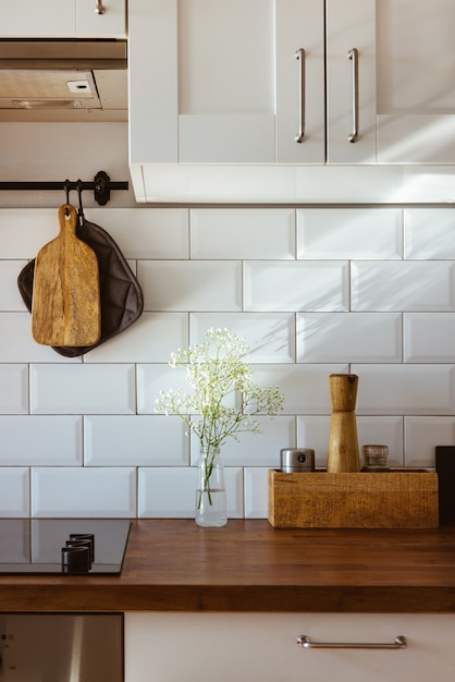 Messing keukengerei, chef-kok accessoires. Hangende keuken met witte tegelsmuur en houten tafelblad. Witte bloemen op keukenachtergrond vroeg in de ochtend licht zijaanzicht