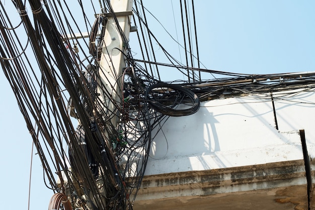 Messy chaos of cables with wires on electric pole and blue sky