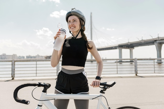 Met behulp van een sportwaterfles traint een vrouwelijke fietser overdag in een helm Gezonde levensstijl