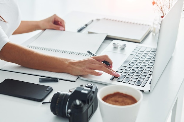 Met behulp van laptop en notitieblok Jonge vrouwelijke freelancer die overdag op kantoor werkt