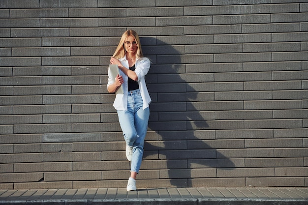 Met behulp van laptop Mooie blonde in vrijetijdskleding is buiten op zonnige dag