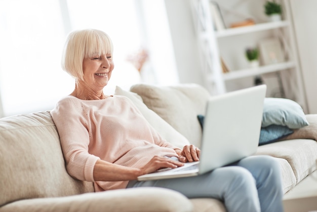 Met behulp van moderne technologieën. Mooie senior vrouw die laptop gebruikt en glimlacht