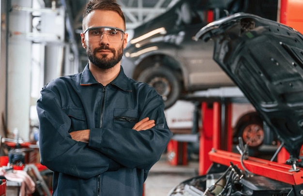 Met de armen gekruist staat de auto-reparateur in de garage met de auto