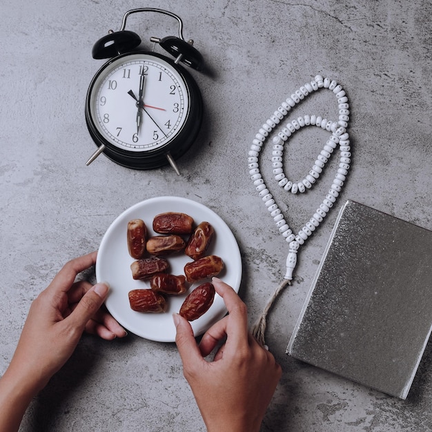 Met de hand genomen dadelfruit, gerangschikt met wekker met iftar-tijd, gebedskralen en Al Quran.