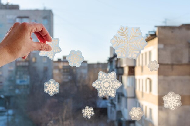 Met de hand plakken van handgemaakte sneeuwvlokstickers op het raam van een huis, close-up, uitzicht vanuit het raam. sneeuwvlokpatroon op vensterglas. kerst huisdecoratie concept.