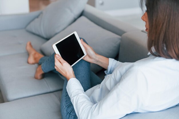 Met digitale tablet in handen Jonge vrouw is overdag binnenshuis in de kamer van een modern huis