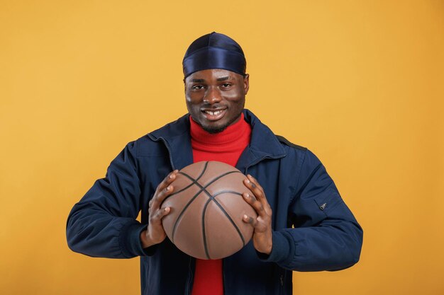 Foto met een basketbal. een knappe zwarte man is in de studio tegen een gele achtergrond.