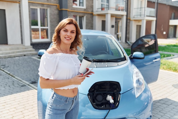 Met een kopje drank Jonge vrouw in vrijetijdskleding met haar elektromobiel overdag buiten